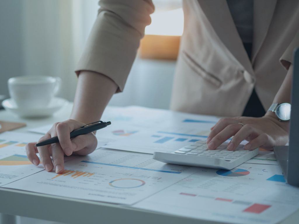 Back Office and Remote Workforce services image of printed financial documents with a hand on a calculator